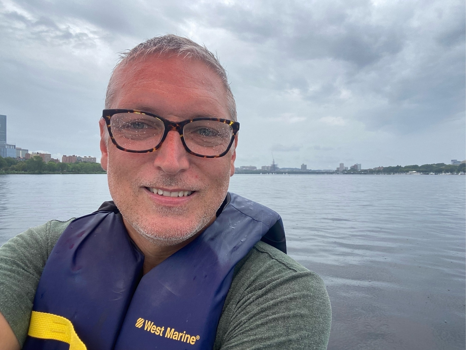 selfie wearing a life jacket with glasses sprinkled with water. open water behind.