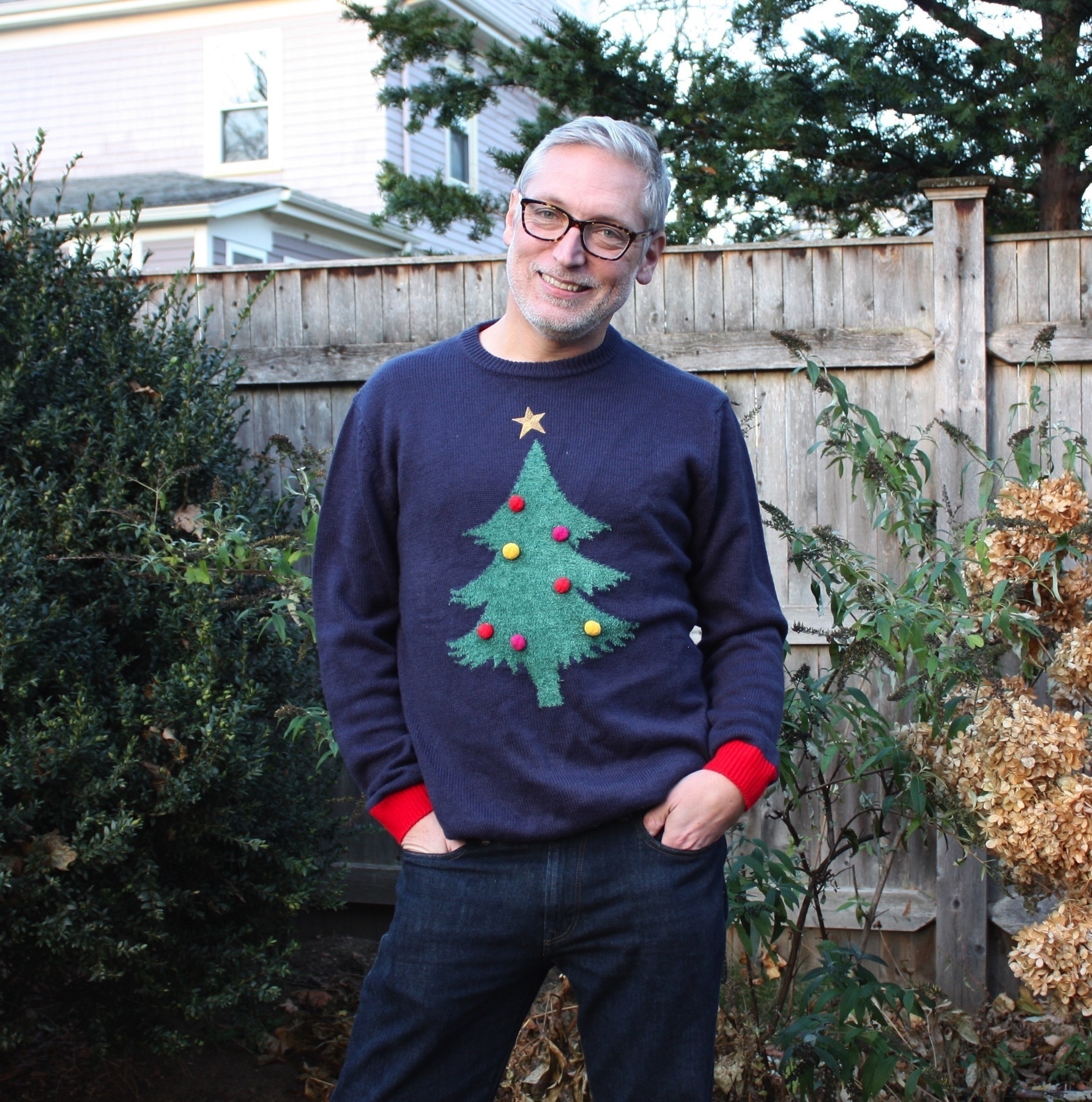 Picture of me outdoors wearing a Christmas tree novelty sweater, standing with weight shifted to one leg and hands in pockets.