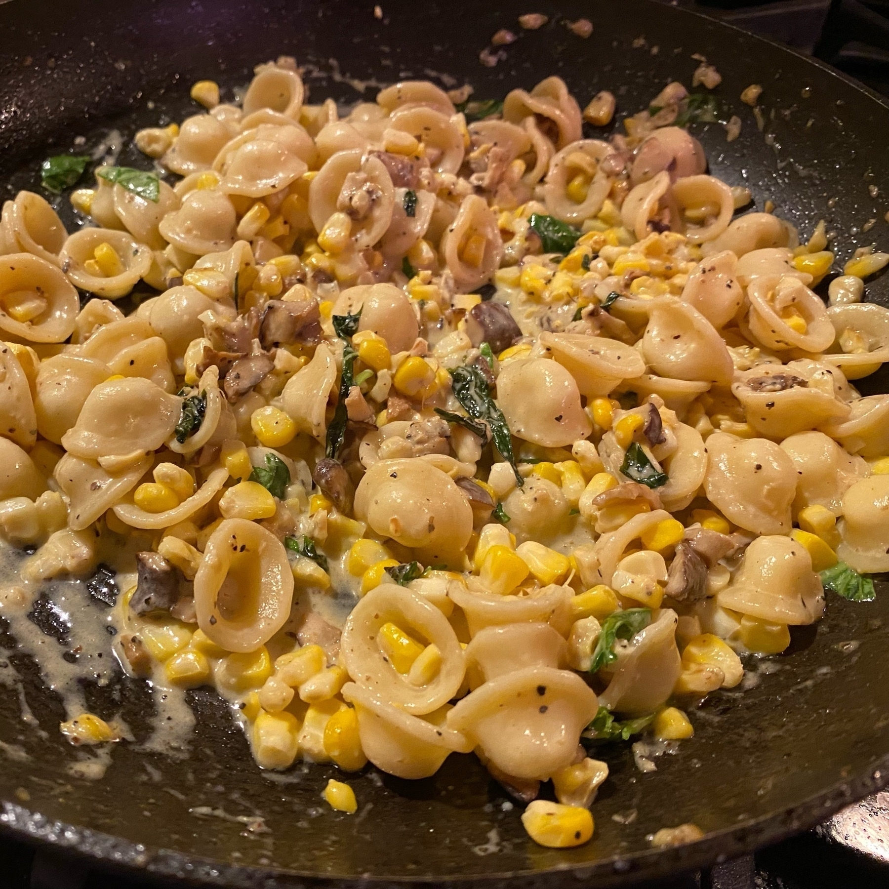 picture of a pan with pasta and corn, mushrooms, basil, cream