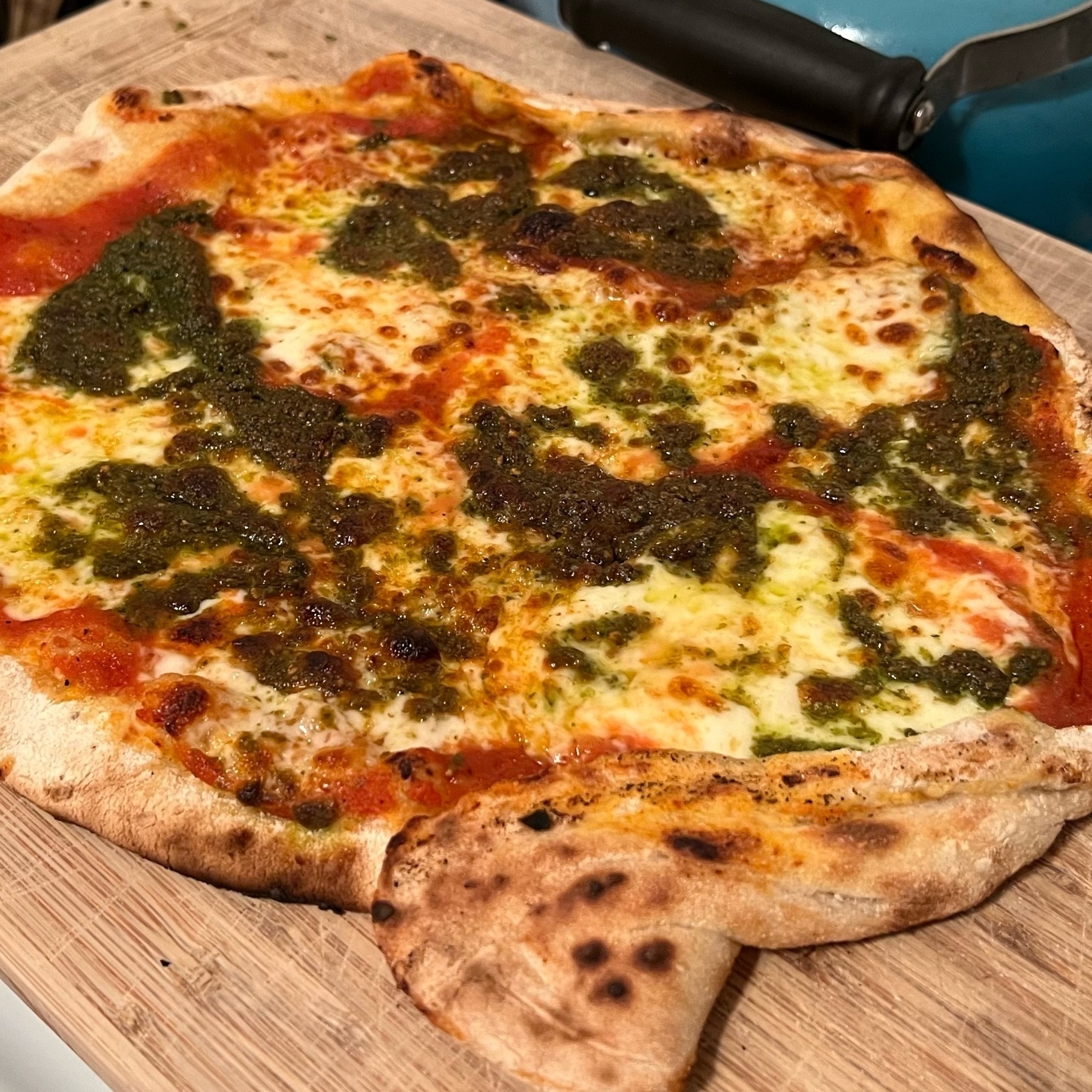 picture of a home baked cheese and pesto pizza with an irregular shape