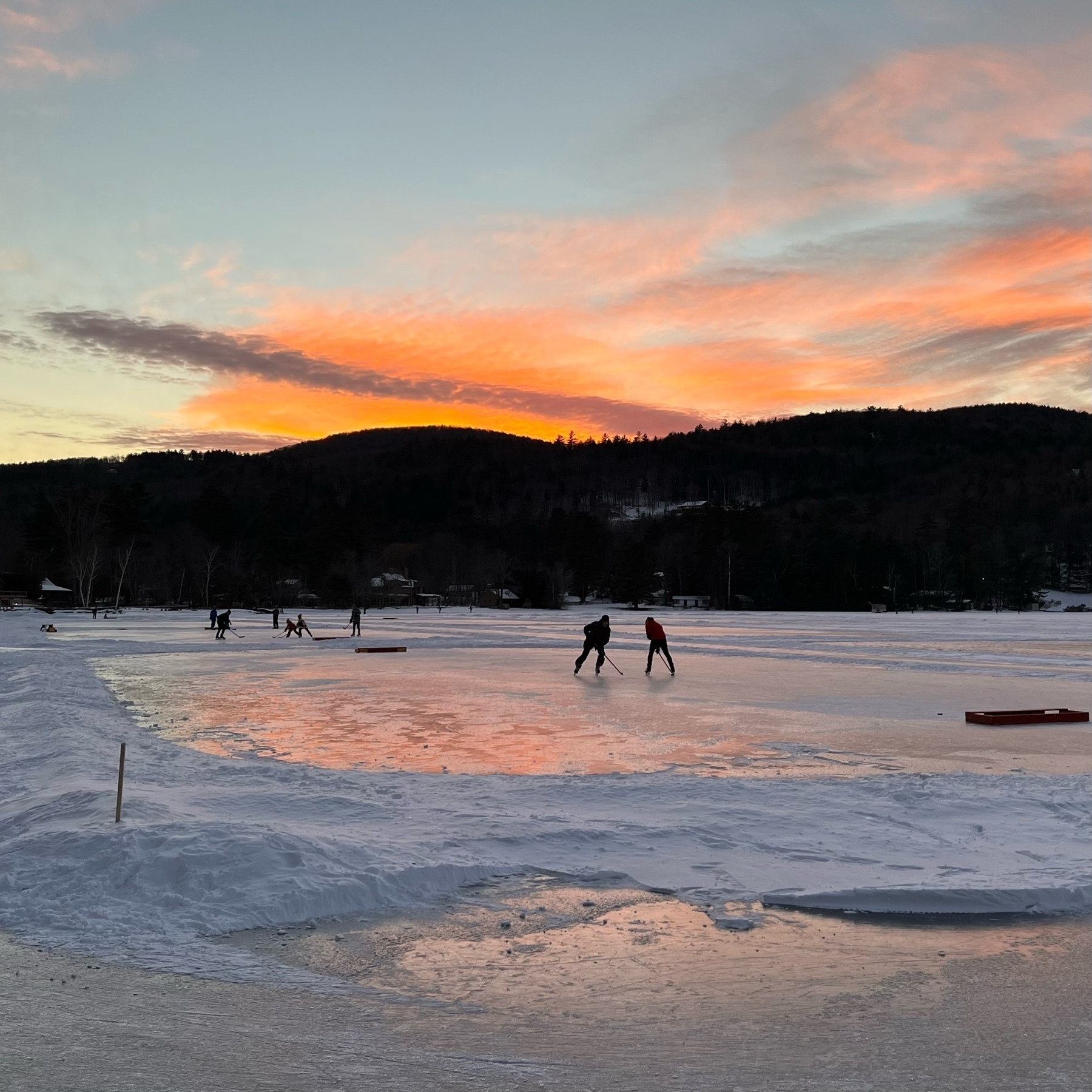 sunset picture on a frozen lake with hockey players and other skaters