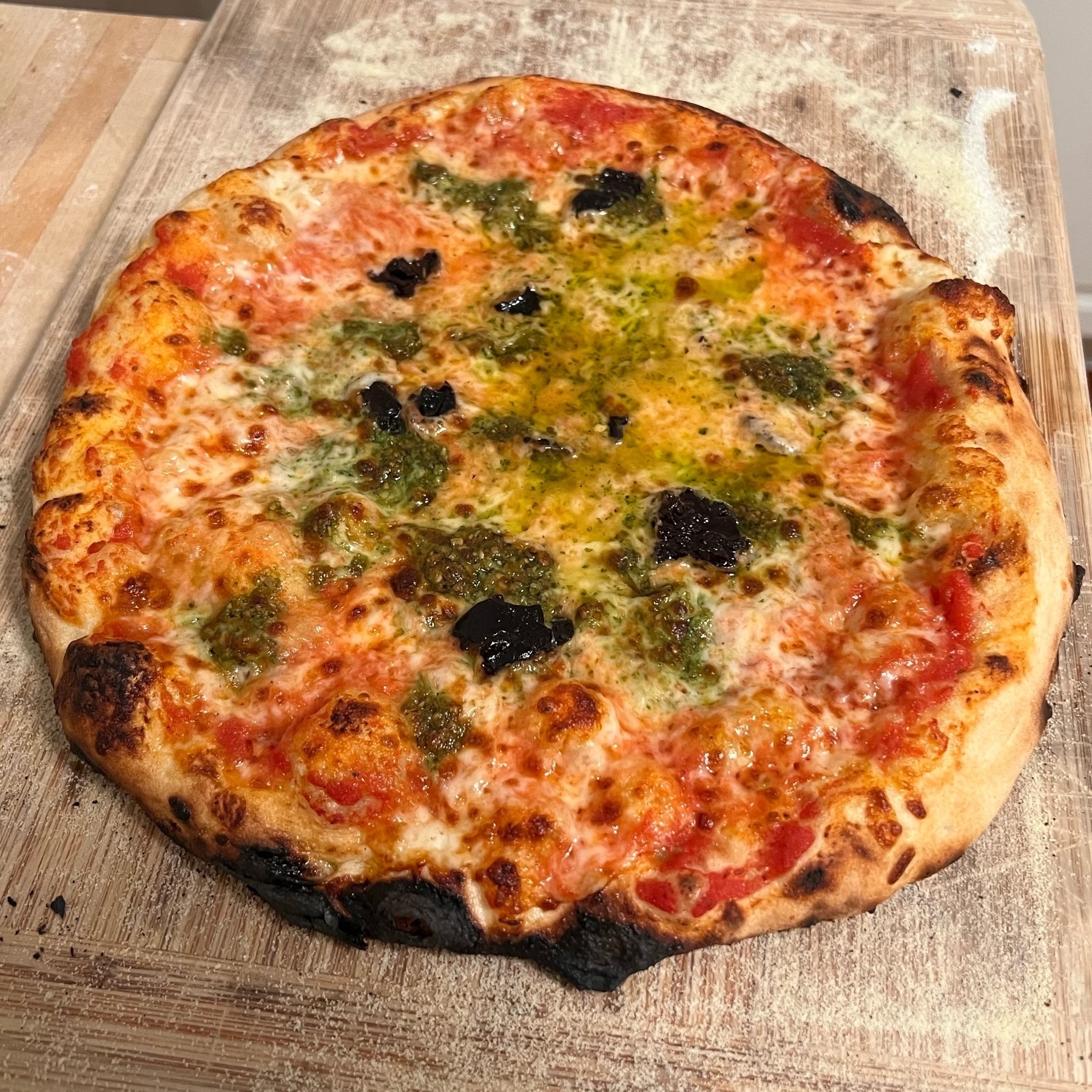 picture of a homemade pizza with green splotches of pesto and dots of black olives