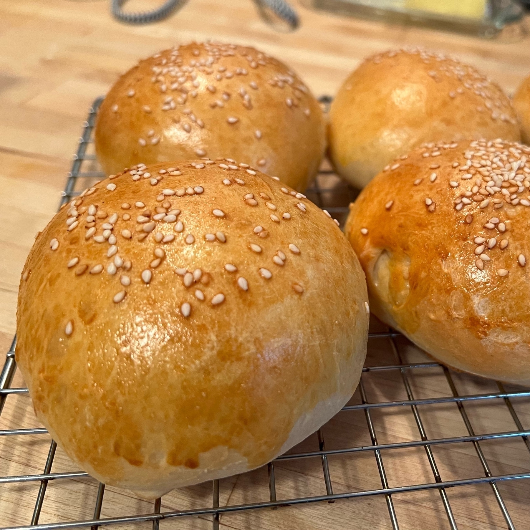 fresh baked, well-risen hamburger buns with a shine from egg wash, and sesame seeds.