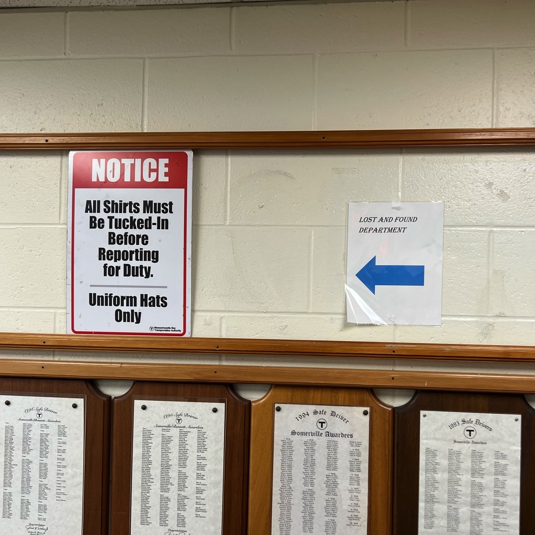 Picture of an interior office building wall with a sign "All shirt must be tucked in before reporting for duty" next to a sign with an arrow "Lost and Found Department"