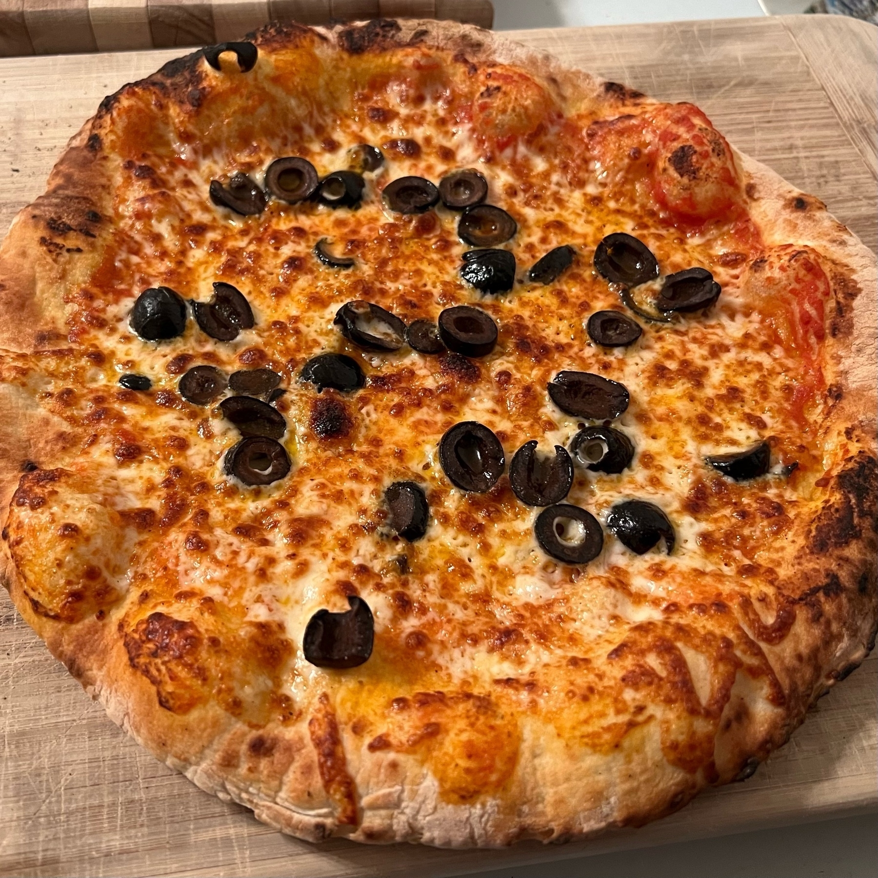 olive and cheese pizza with puffy crusts resting on a wooden cutting board